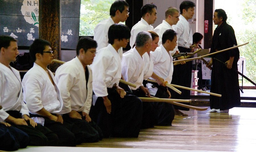Practicantes de artes marciales japonesas tradicionales arrodillados durante una práctica con armas en un dojo